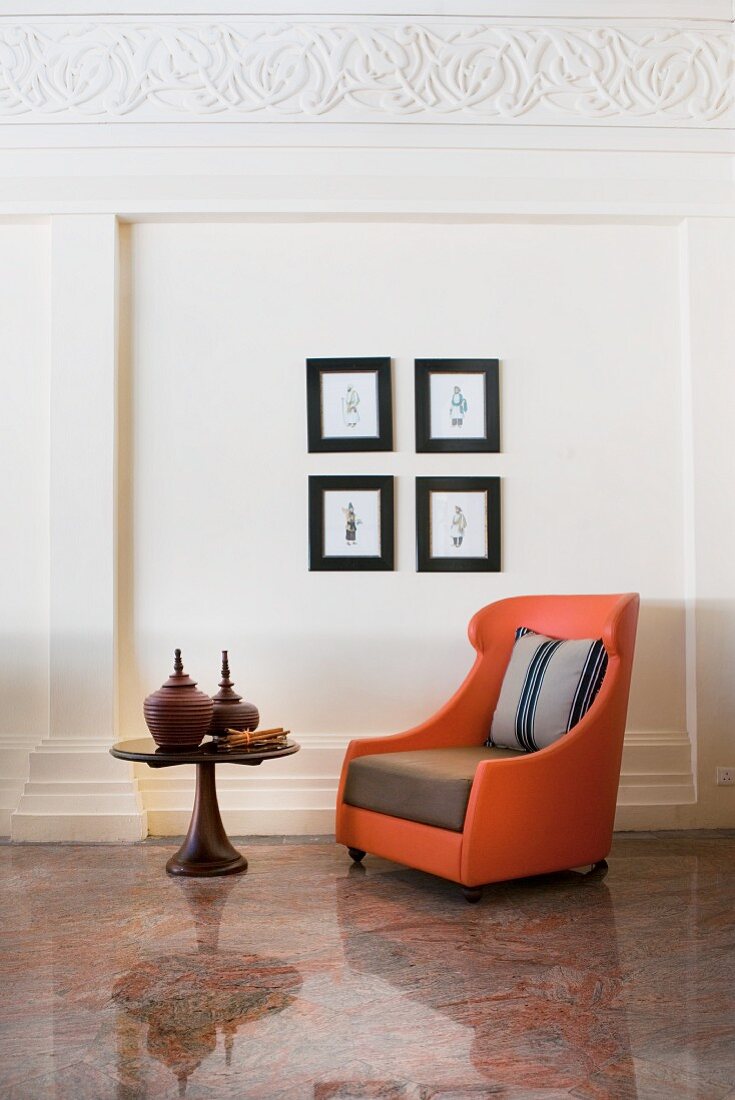 Orange armchair on stone floor below pictures on wall