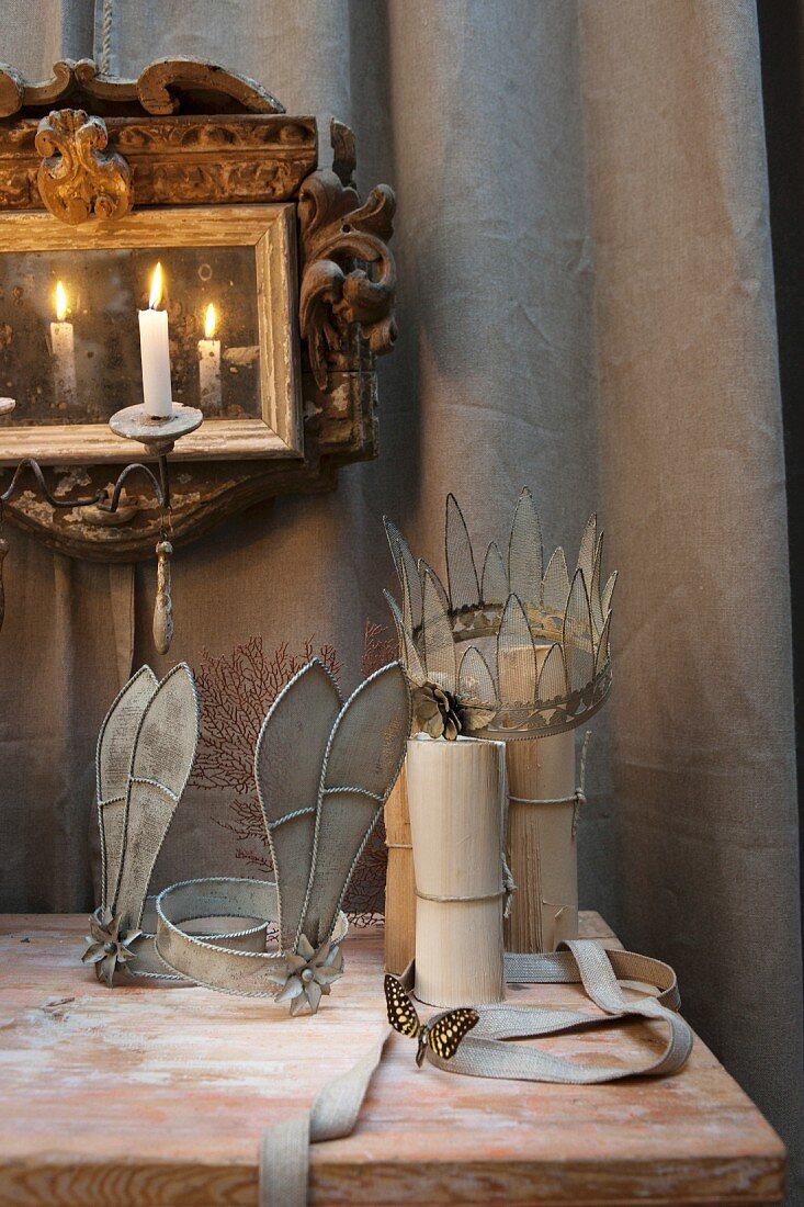 Arrangement mit kunsthandwerklichem, nostalgischem Kopfschmuck vor Goldrahmenspiegel mit Kerzenlicht