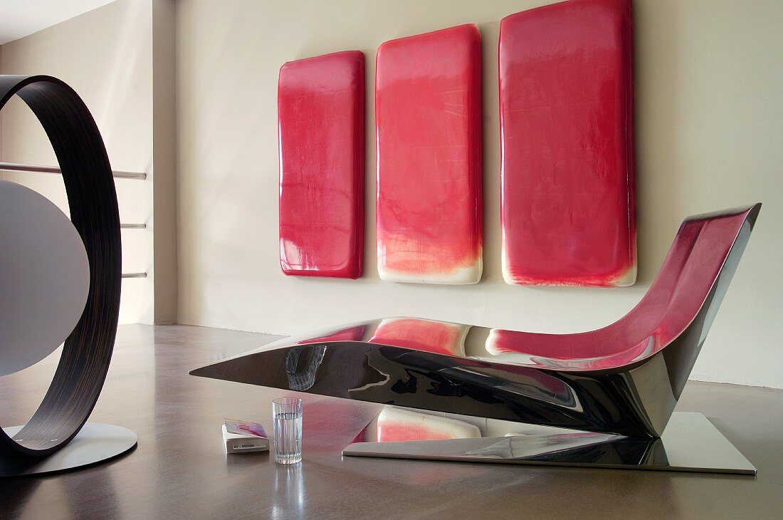Designerliege aus spiegeldem Metall vor rotem Kunstwerk