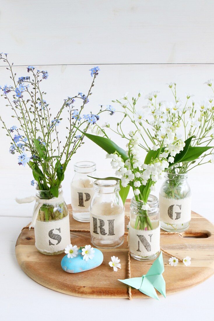 Frühlingsblumen in Gläsern mit Stoffbanderole und Buchstaben