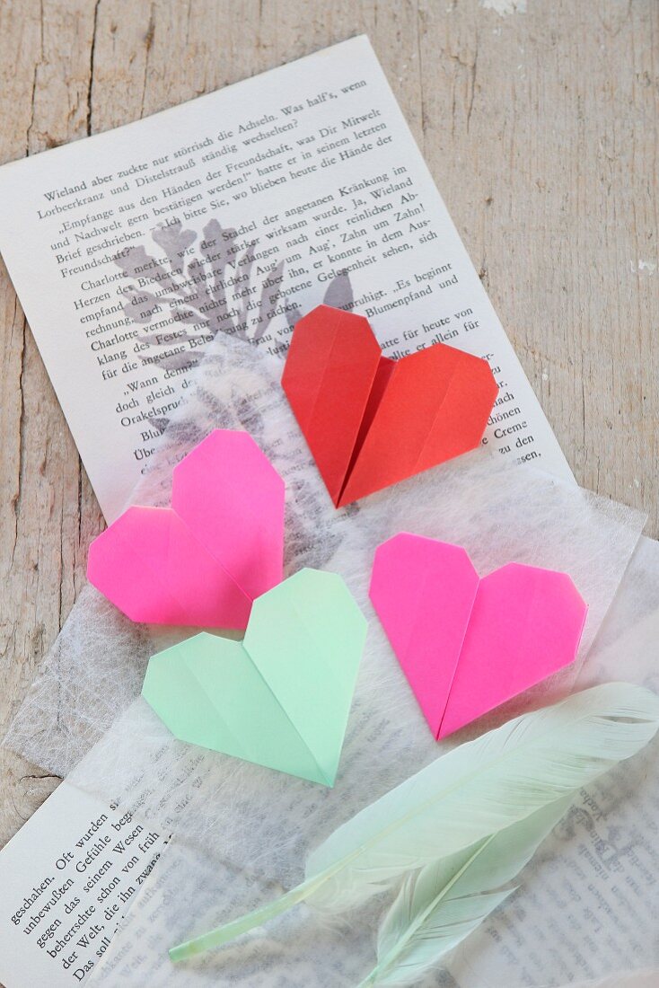 Origami hearts and feathers on book pages and tissue paper