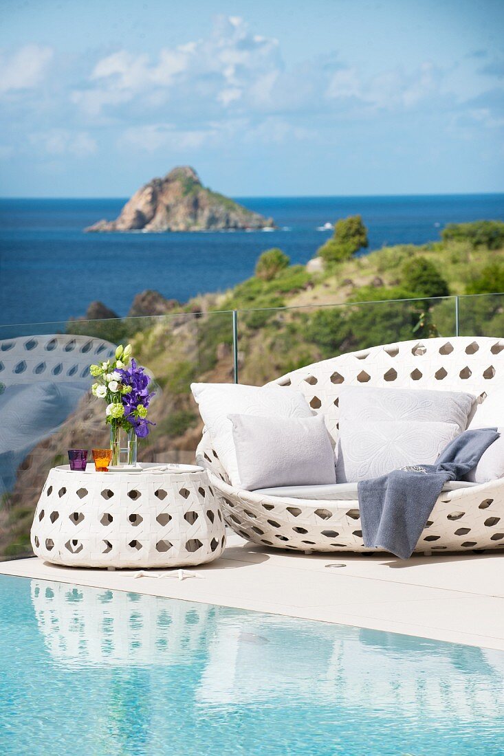 weiße Outdoormöbel am Pool mit Blick aufs Meer und eine Insel