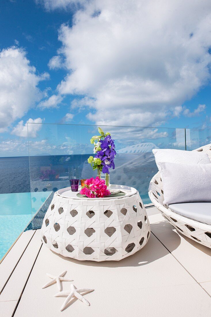 Flowers on white side table in front of sea and clouds in blue sky