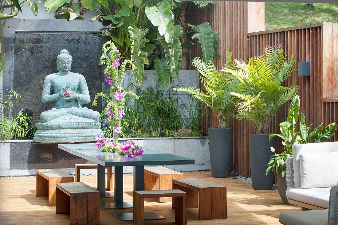 Potted palms, Buddha statue, stools and table on exotic terrace