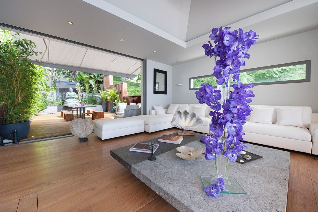 Vertical flower arrangement in living room with open glass wall leading to terrace
