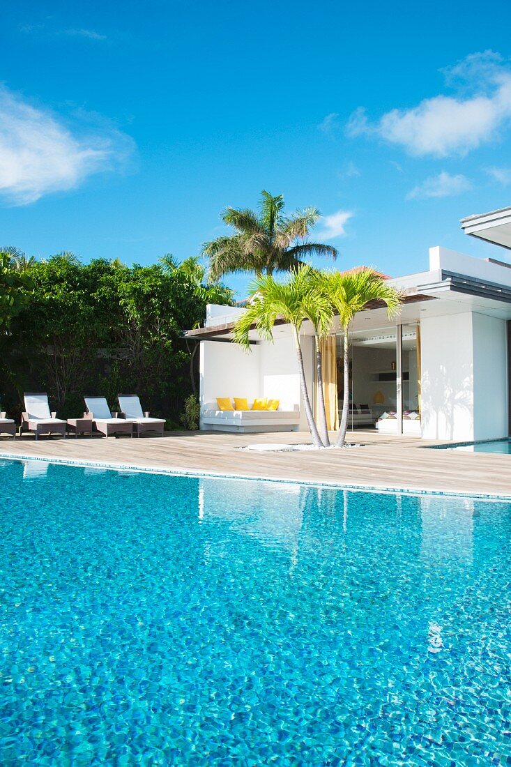 Terrasse am Pool mit Palmen unter blauem Himmel