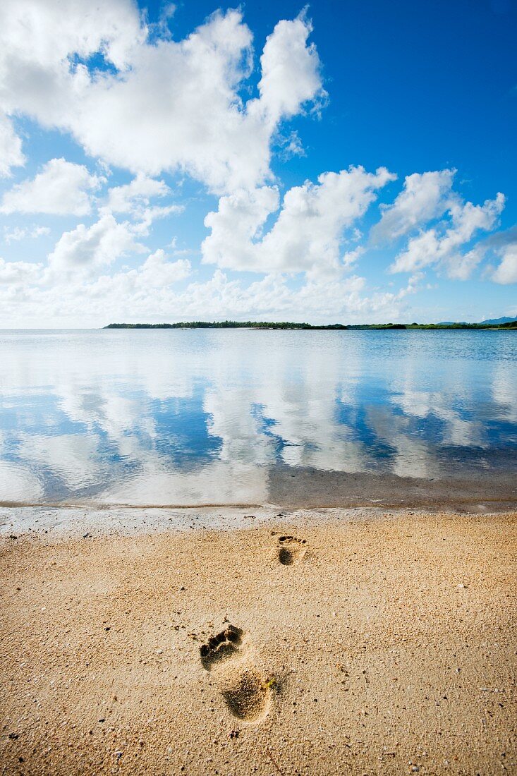 Fußspur auf Sand am Meer unter blauem Himmel mit weissen Wolken