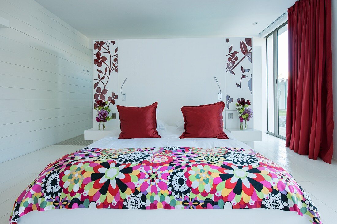 Red accents and floral patterns in white bedroom