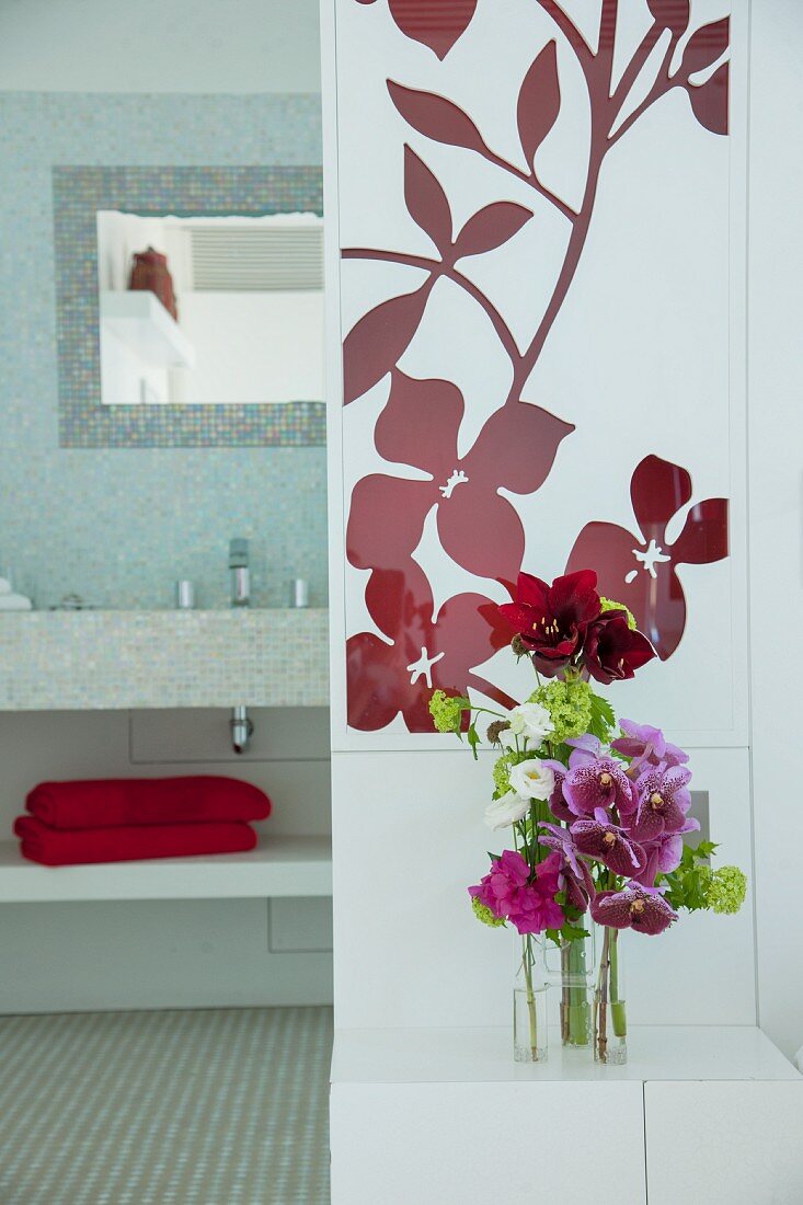 Flowers on bedside table and view into bathroom with mosaic tiles