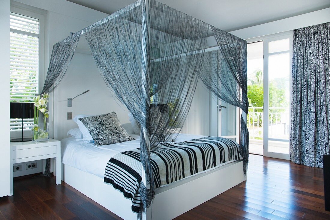 Four-poster bed with string curtains in black and white bedroom
