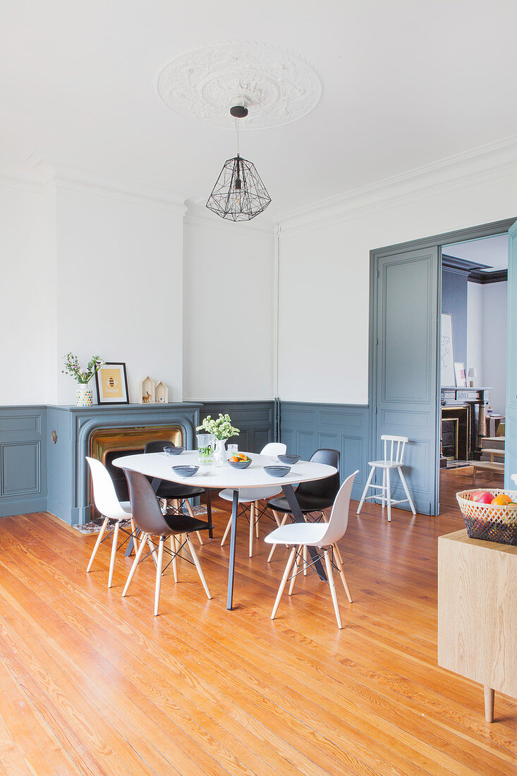 Esstisch mit Stühlen vor Kamin im Wohnraum mit weissen Wänden und grau-blauer Vertäfelung im Sockelbereich