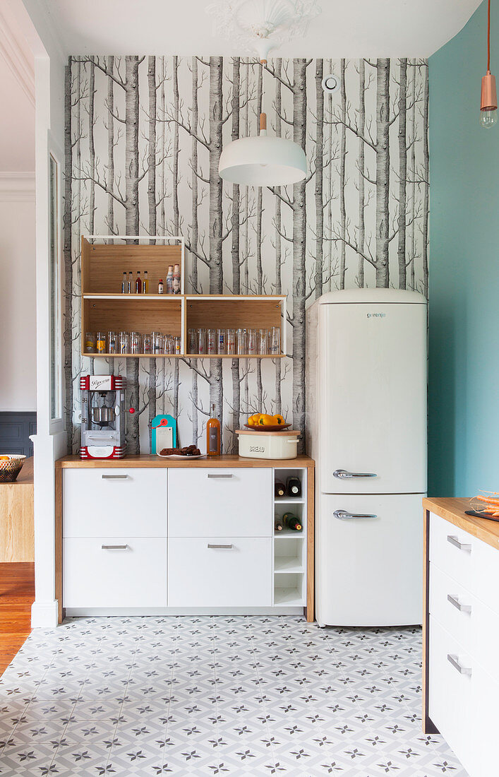 Unterschrank und weisser Kühlschrank vor Tapete mit Baummotiv in der Küche, Zementfliesen auf dem Boden