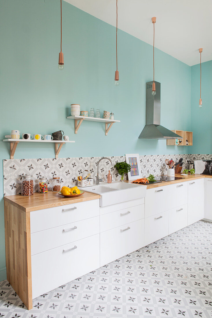 Küche mit weissen Schrankfronten, hellblauer Wand und gemusterten Zementfliesen