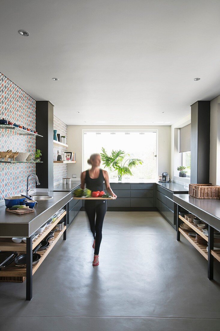 Frau trägt Tablett durch große moderne Küche in Grautönen