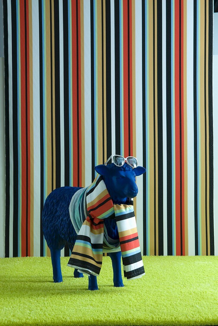 Blue sheep statue wearing scarf and sunglasses in front of striped wall