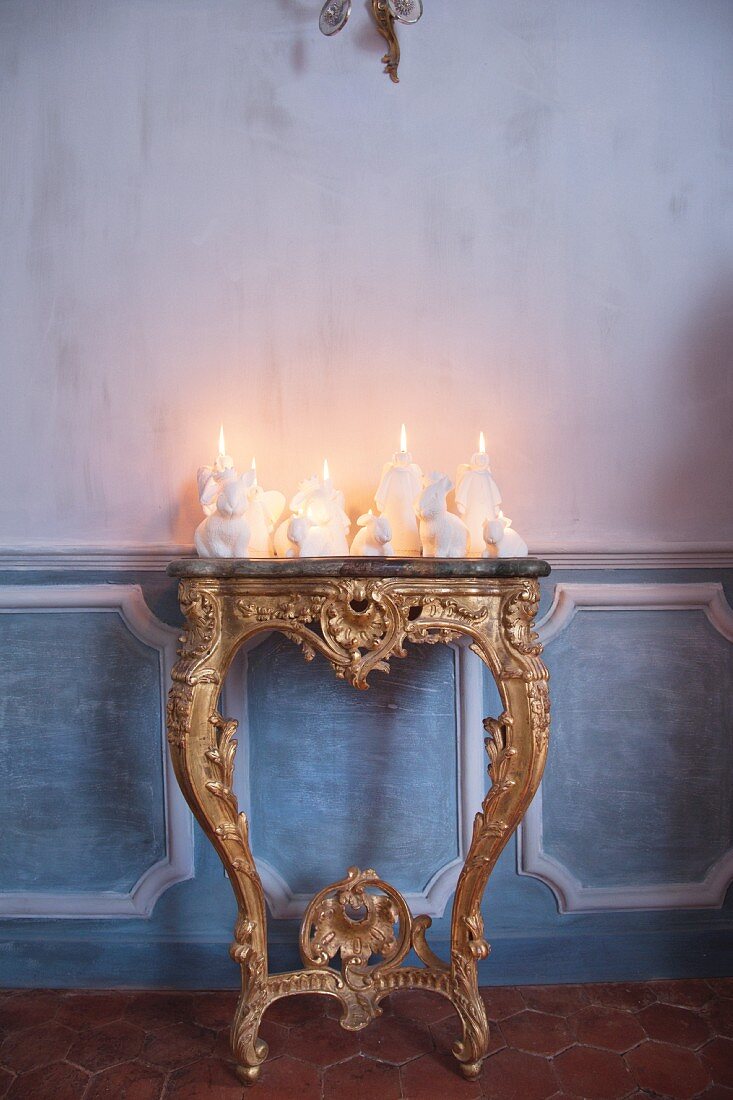 Arrangement of white candles of various shapes on antique gilt console table