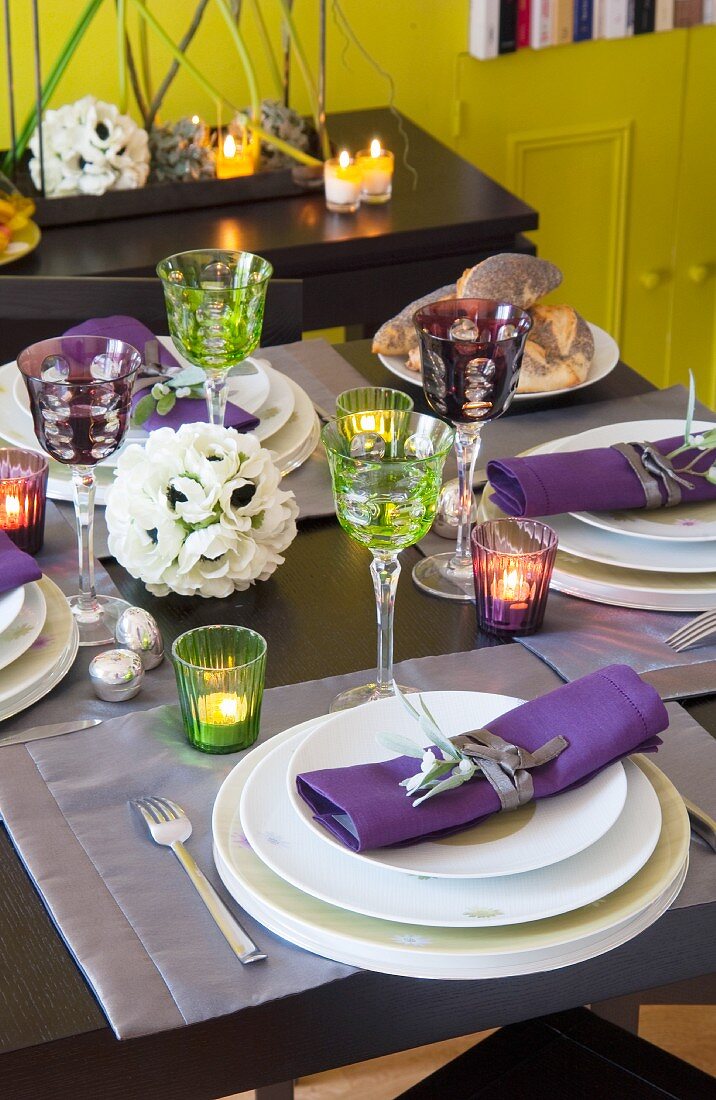 Festliche Tischdekoration mit Dekoblumen, brennenden Teelichtern und eleganten, bunten Weingläsern