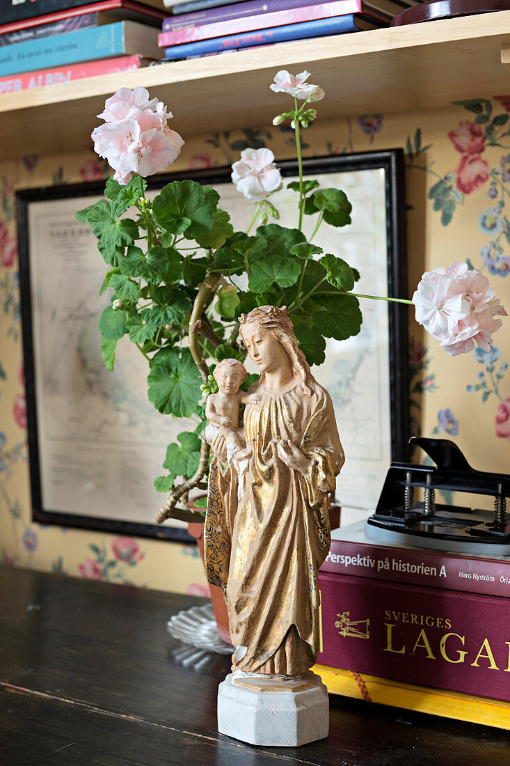 Religious figurine, potted geranium and books on desk