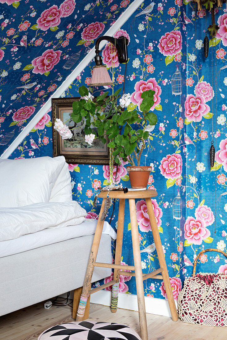 Stool next to bed under sloping ceiling covered with floral wallpaper