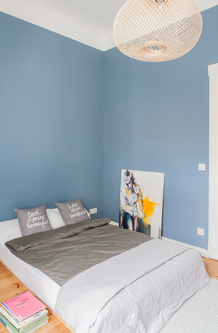 Double bed and modern art in bedroom with blue wall
