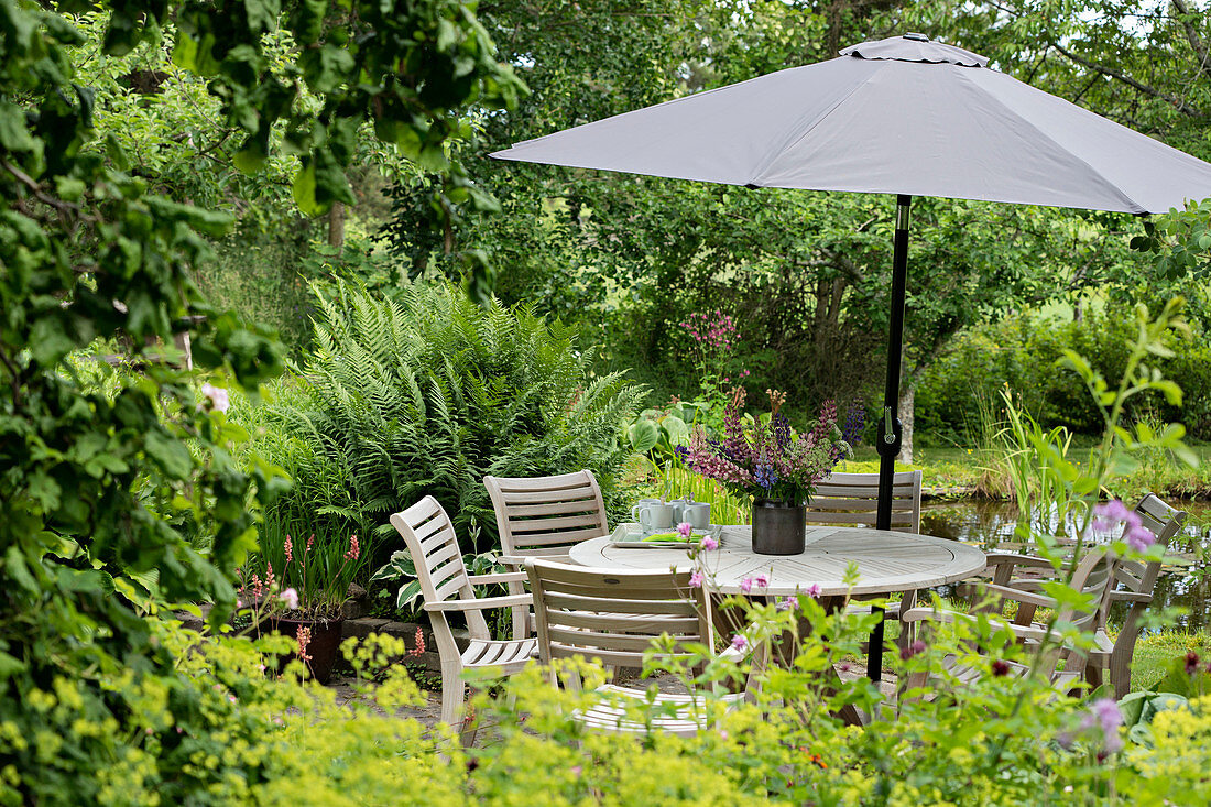 Round table, chairs and parasol on terrace in densely planted garden