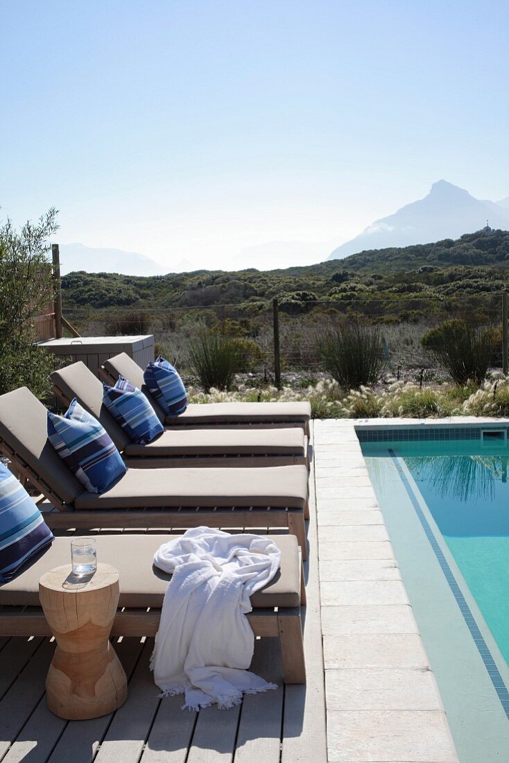 Upholstered sun loungers next to pool with view of summery landscape