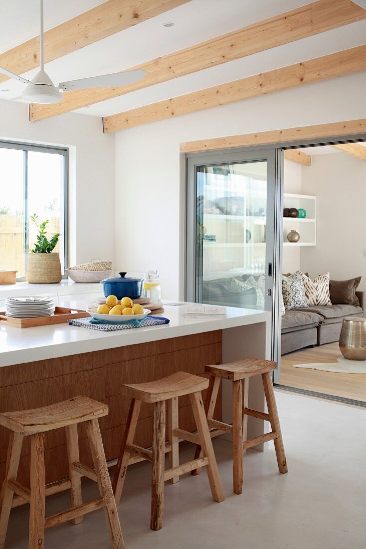 Rustic bar stools at white kitchen counter with view into living area