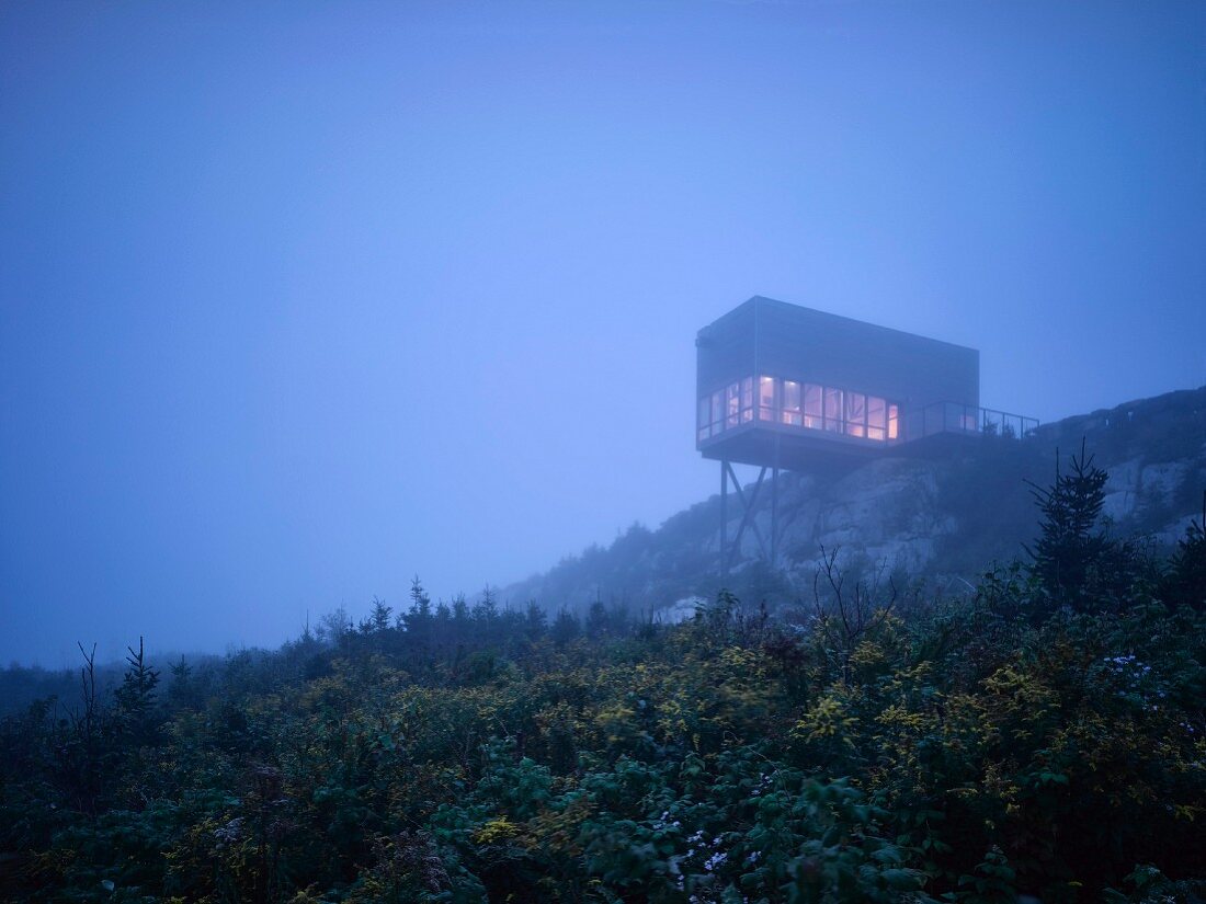 Modern cubist house protruding out from hilltop in the fog