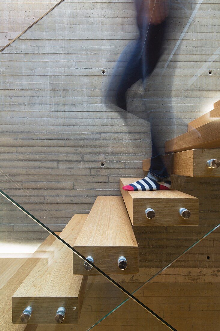 Person geht auf schwebender Treppe mit Glasgeländer