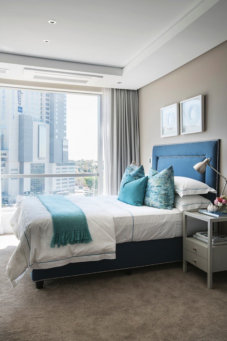 Elegantes Schlafzimmer mit blauem Polsterbett und beigem Teppichboden