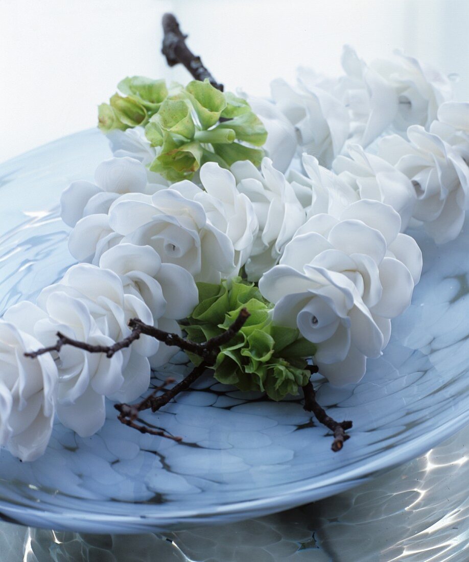 White china flowers, green flowers and twig in dish