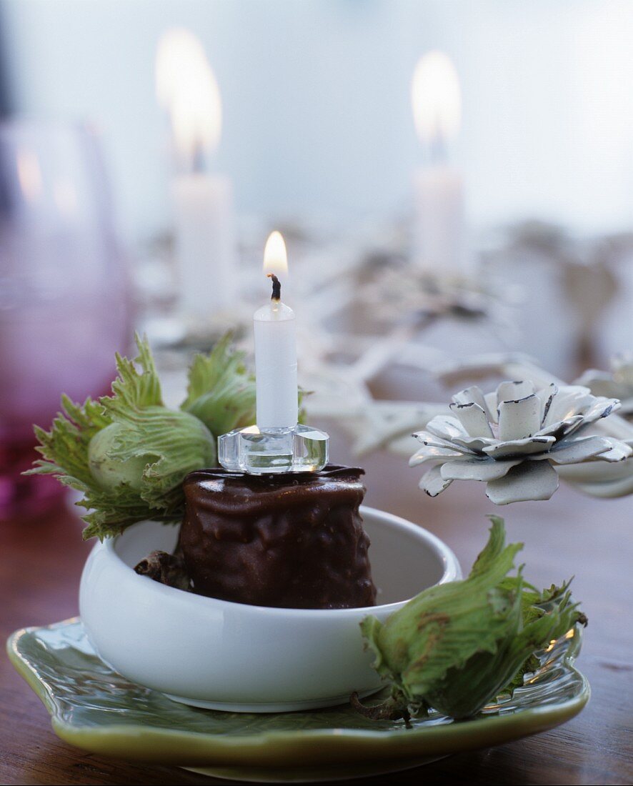 Candle in chocolate desert decorated with green hazelnuts