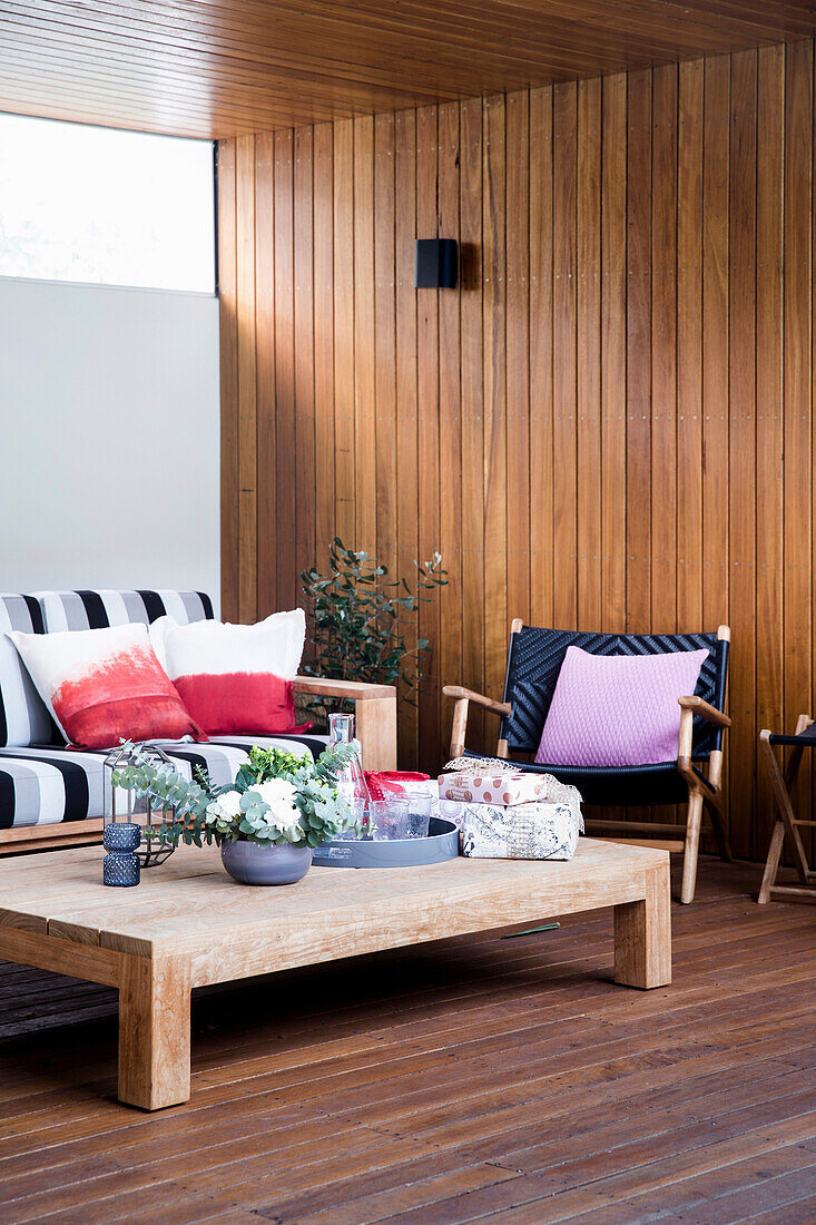 Niedriger Couchtisch, Sessel und Sofa mit Kissen auf überdachter Terrasse