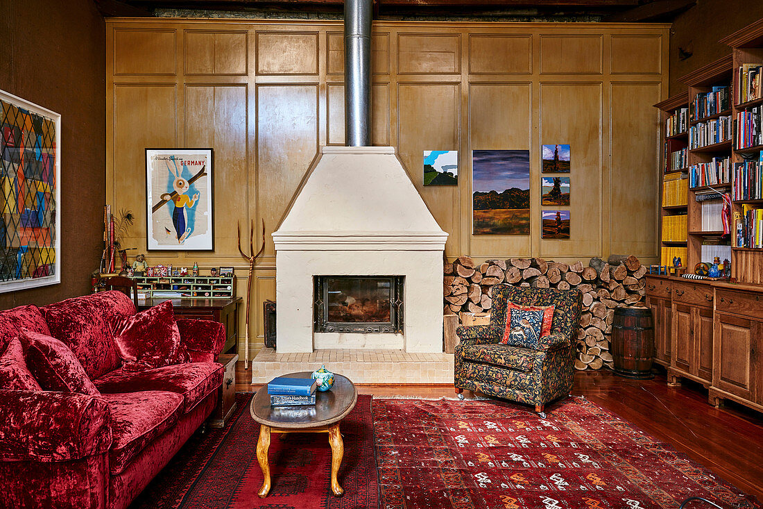 Upholstered armchairs in front of wood storage, fireplace and red sofa with velvet upholstery in the living room