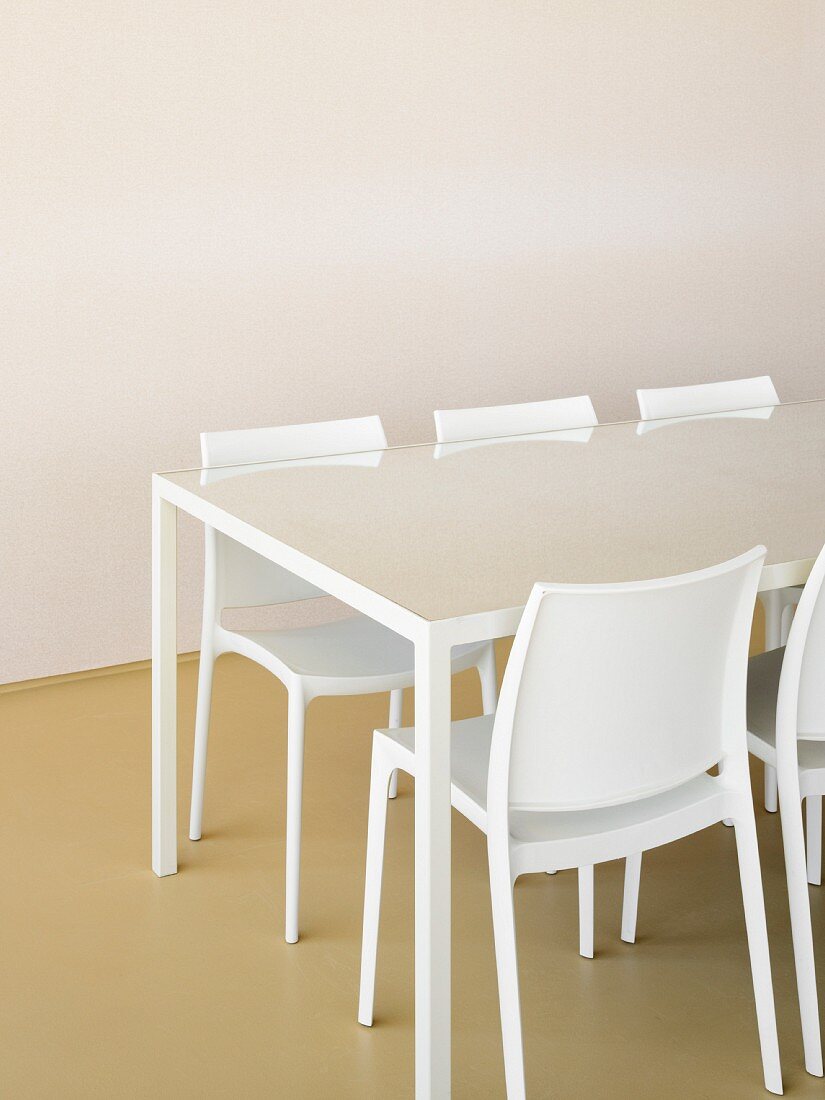 Weißer Tisch mit Glasplatte und Designerstühlen vor leerer Wand