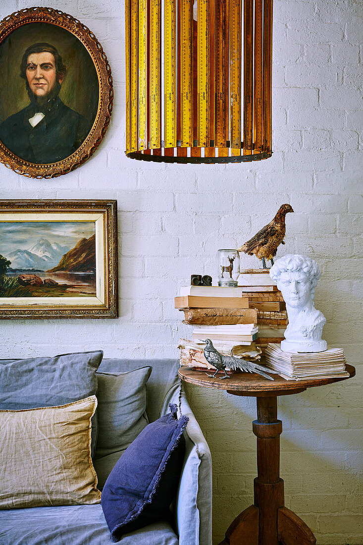 Antique wooden table with bust, books and bird figures next to sofa in living room with white painted brick wall