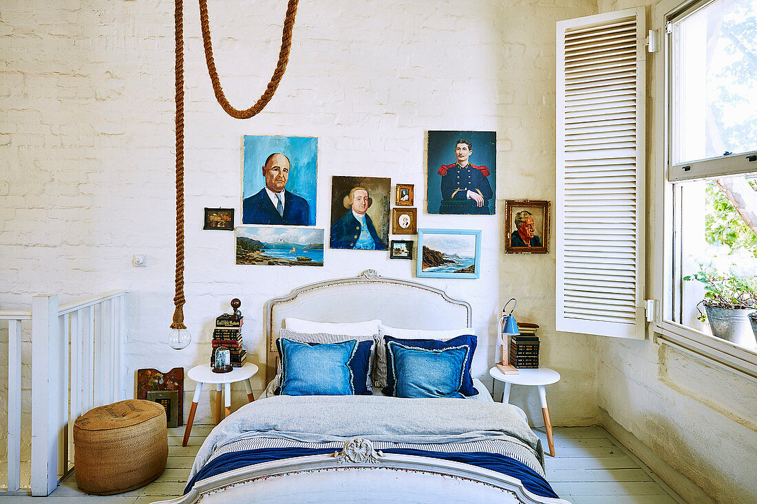 Doppelbett mit blauen Kissen und Portraitmalerei an weiß gestrichener Ziegelwand