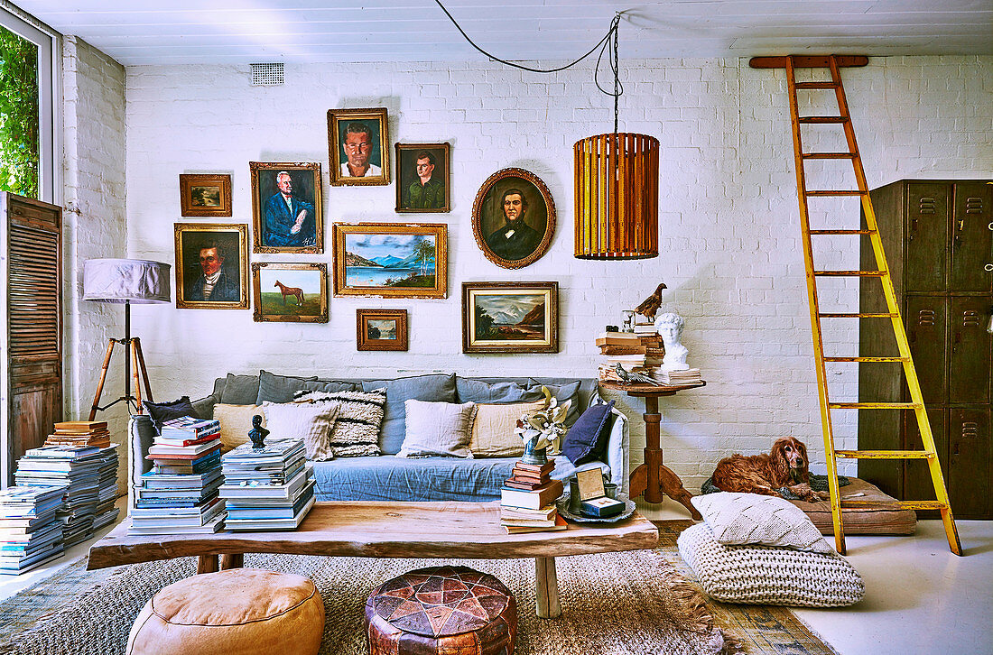 Holztisch mit Bücherstapel, Sofa und Bildergalerie im Vintage Wohnzimmer mit weiß gestrichener Ziegelwand