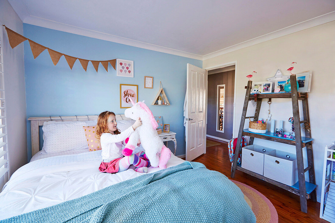 Mädchen spielt auf dem Bett, DIY-Regal aus alter Holzleiter im Kinderzimmer mit hellblauer Wand