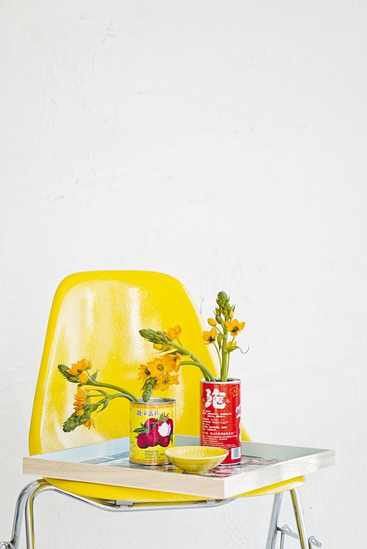 Konservendosen als Blumenvasen auf Tablett und gelbem Stuhl