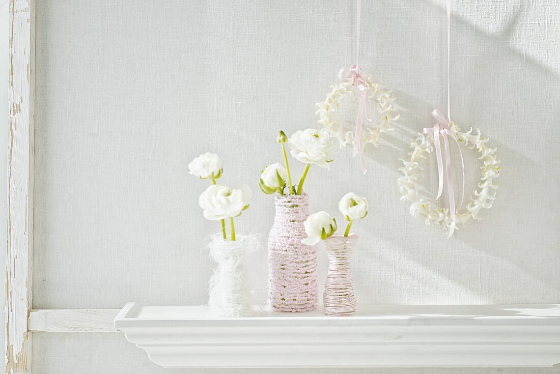 Umwickelte Glasfläschchen mit weißen Ranunkelblüten und Blütenkränze an Seidenbändern