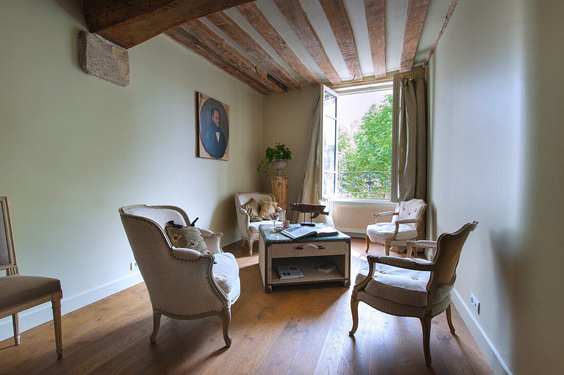 Loungebereich mit antiken Sesseln vor offenem Fenster unter rustikaler Holzbalkendecke