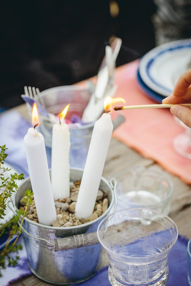 Angezündete, weiße Kerzen in Zink-Eimerchen als Tischdekoration