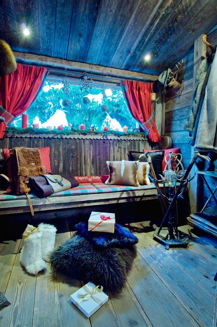 Fur cushions on wooden bench and wrapped Christmas gifts below window in chalet