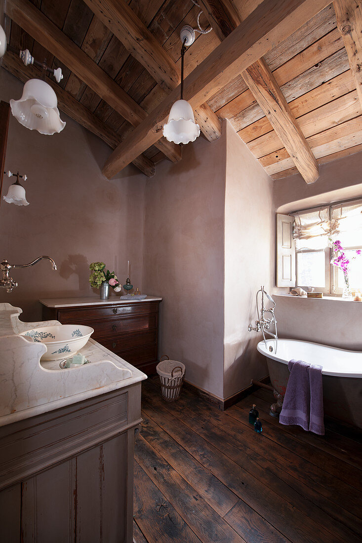 Antique furniture in vintage-style bathroom below exposed roof beams