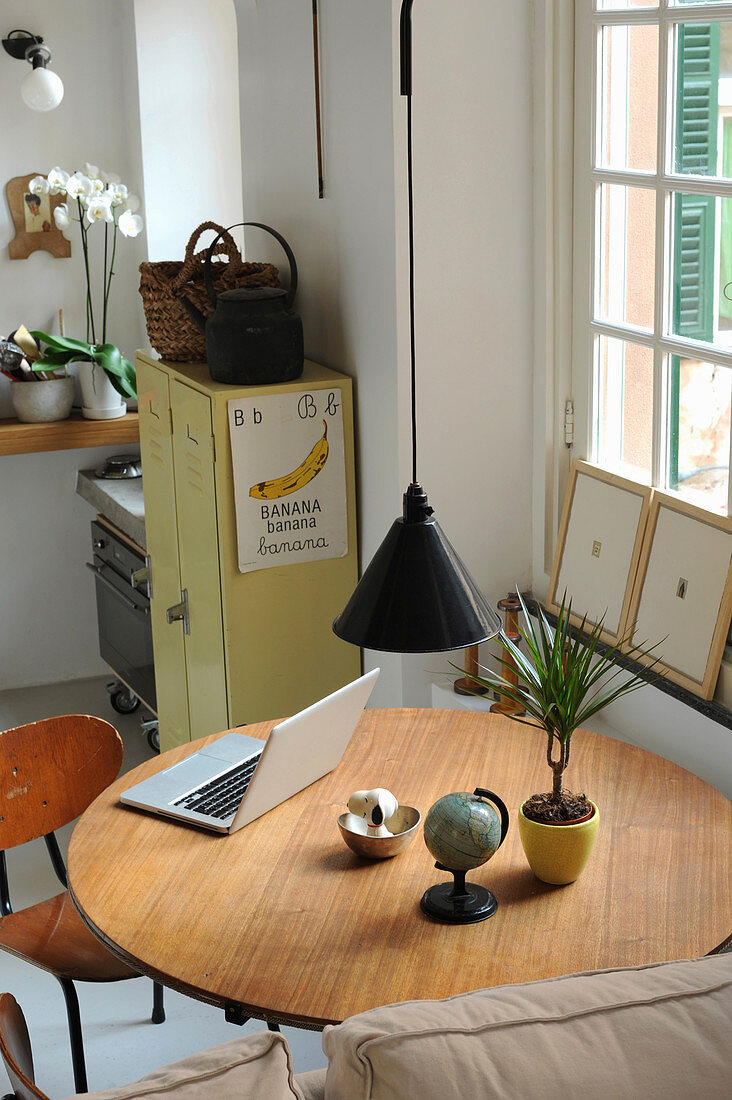Runder Tisch mit Laptop, Zimmerpflanze und kleinem Globus unter Pendelleuchte