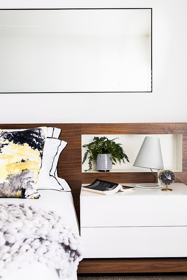 Doppelbett mit elegantem Betthaupt aus Holz und Nachtkästchen, darüber großer Spiegel im Wohnzimmer