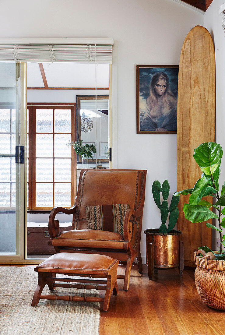 Vintage leather armchair with ottoman next to house plants and surfboard in corner of room
