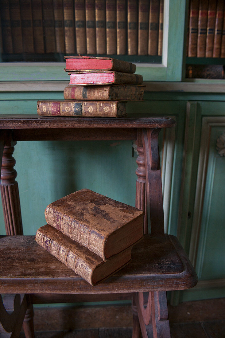 Antiquarian books on old wooden steps in front of bookcase