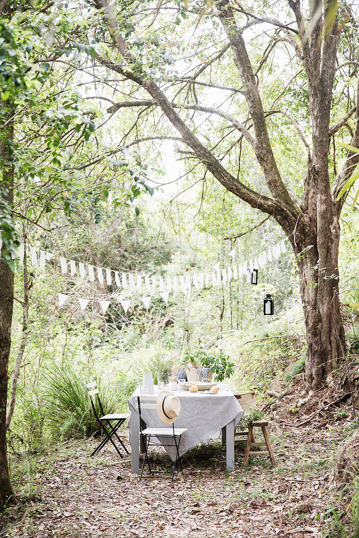 Gedeckter Gartentisch und Stühle unter Wimpelkette im Garten mit hohen Bäumen
